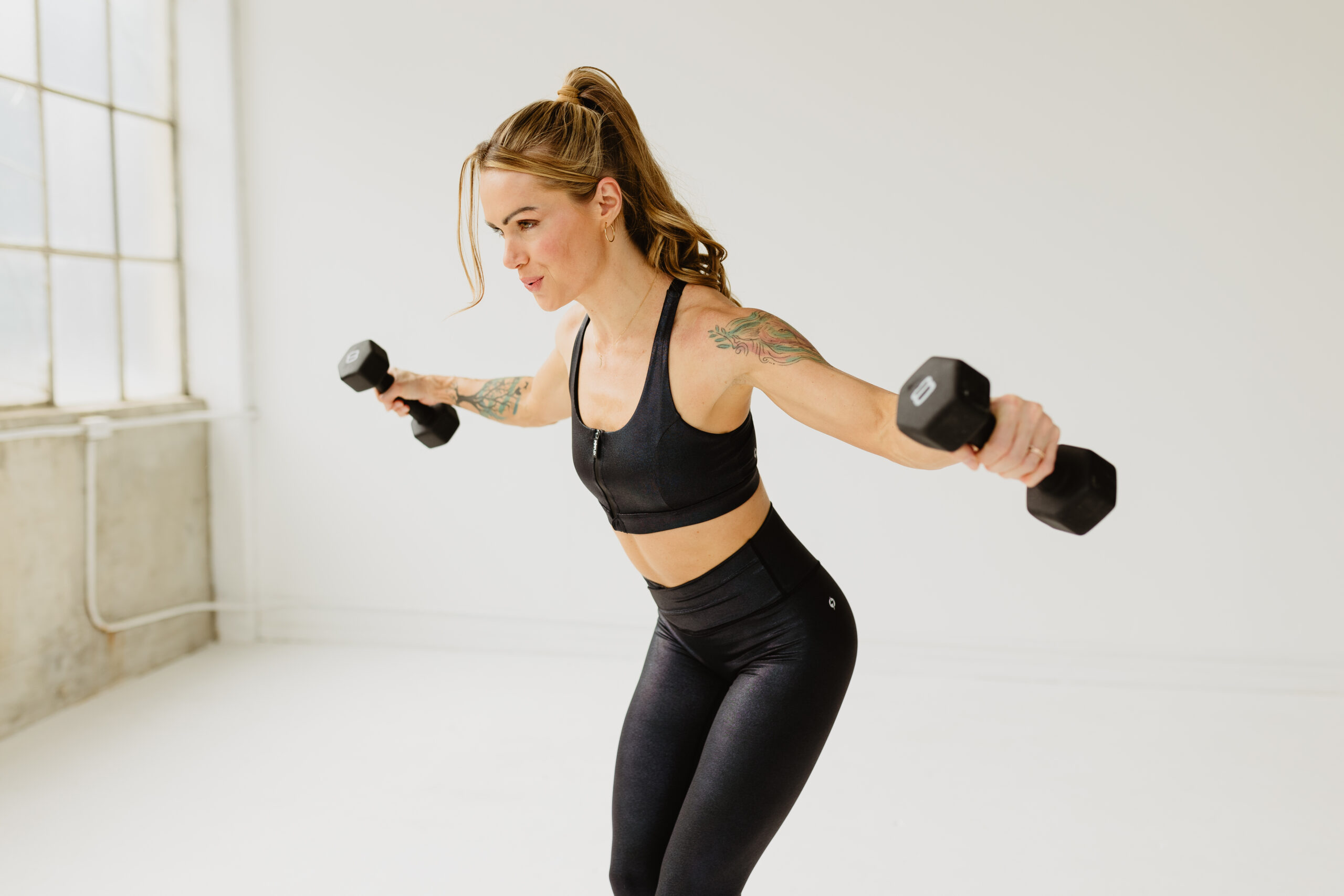 Woman performing shoulder flies with dumbbells—Barre vs. Pilates? Choose both.